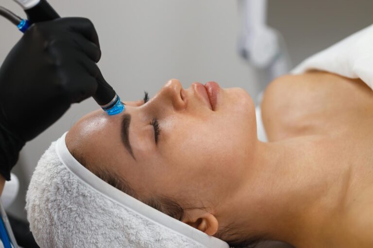 Aesthetician gliding a HydraFacial wand across a woman's cheek during a HydraFacial treatment.